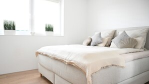 Ein Bett mit Kopfteil, ein Fenster mit Pflanzen und ein Holzboden.