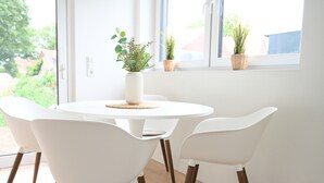 Ein runder, weißer Tisch mit vier weißen Stühlen, eine weiße Vase mit Grünpflanzen und Blick ins Grüne.