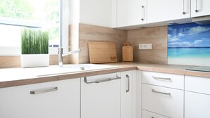 Eine moderne Küche mit weißen Schränken, einer Holz Arbeitsplatte, einem Spülbecken und einem Fenster mit Blick ins Grüne.