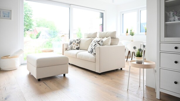 Ein modernes Wohnzimmer mit einer Couch, Hocker und einem Essbereich mit Tisch und Stühlen.
