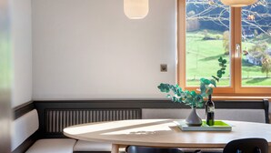 A dining area with a round table, two chairs, a bench, a vase with green foliage, and a bottle. - Holiday Home 'Blueberry Haus Im Moos' with Mountain View, Shared Terrace and Wi-Fi (Oberau)