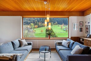 A modern living room with two sofas, a coffee table, and a large window with a view of a green landscape.