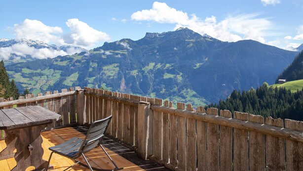 Terraza de madera con una mesa y una silla, con vistas a un paisaje montañoso y una cerca de madera.