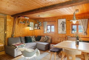 A wooden cabin interior with a sofa, dining table, and a map on the wall.