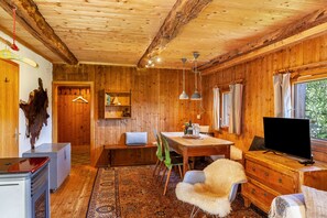 Interior de una cabaña de madera con una mesa de comedor, sillas, un televisor y una lámpara colgante.