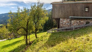 A rustic wooden building with a stone foundation, surrounded by lush greenery and a hillside view. - Apartment 'Ground Floor' with Mountain View, Private Terrace and Garden (Oberau)
