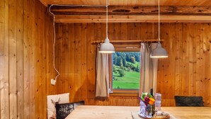 A wooden interior with a dining table, two pendant lights, a window with curtains, and a view of a green landscape. - Apartment 'Ground Floor' with Mountain View, Private Terrace and Garden (Oberau)