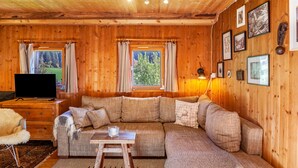 A wooden interior with a sectional sofa, a flat-screen TV, a small table, and framed pictures on the wall. - Apartment 'Ground Floor' with Mountain View, Private Terrace and Garden (Oberau)