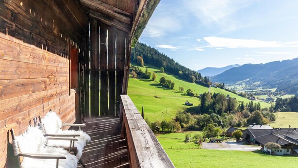 Un edificio de madera con un balcón que da a un valle verde y montañas.