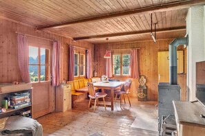 Un intérieur en bois comprenant une table à manger, des chaises, un banc, une bibliothèque et une cheminée.