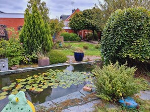 Um jardim com lago, plantas em vasos e um caminho de tijolos.
