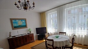 A dining area with a round table, chairs, a television, a painting, and a window with curtains. - Apartment 'Ingrid Bauer 2' with Wi-Fi (Kühlungsborn)