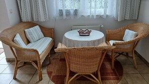 Una habitación con un sofá de mimbre, dos sillones de mimbre, una mesa redonda con mantel de encaje y una alfombra estampada.