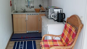 Una cocina compacta con armarios de madera, un lavamanos, un tostador, una cafetera y una silla de mimbre.