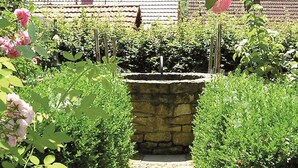 A stone structure in a garden with surrounding greenery and a building with a tiled roof in the background. - Apartment 'Fewo 1' with Wi-Fi (Müllheim im Markgräflerland)