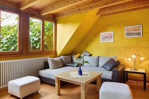 Ein Zimmer mit einer Couch, einem Tisch, einem Heizkörper und einem Fenster mit Blick auf Grünflächen.