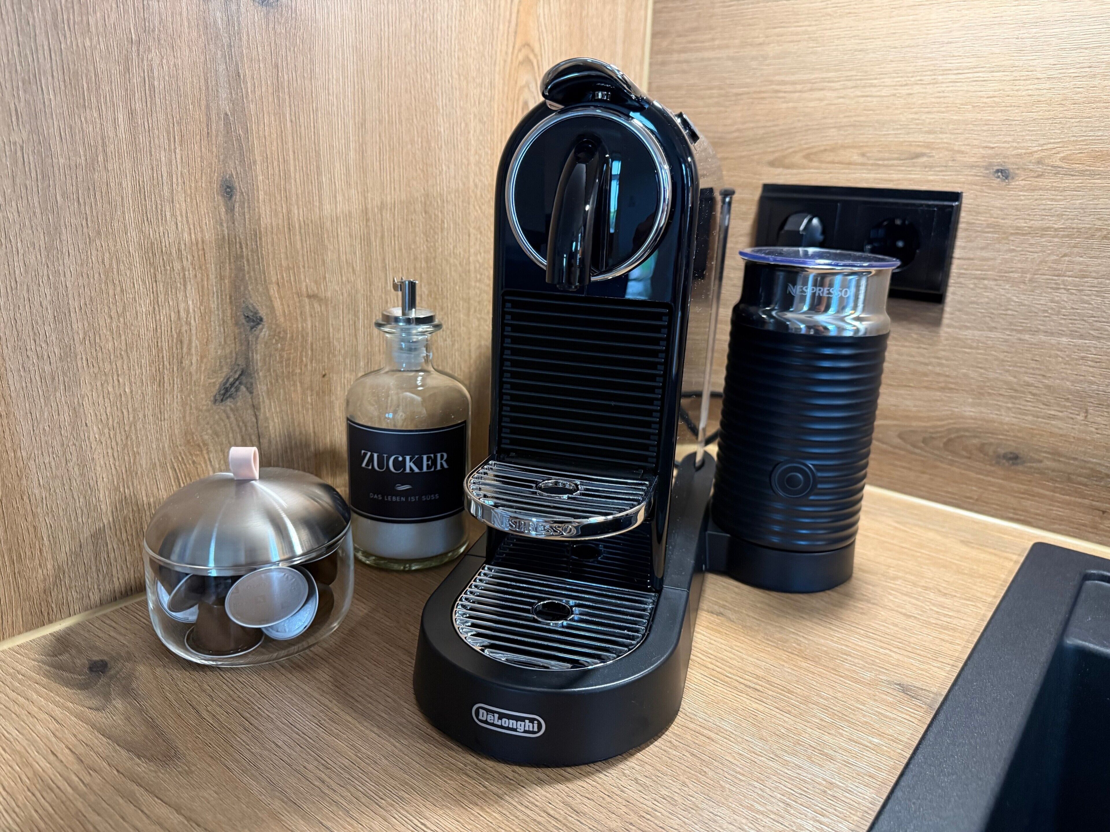 A coffee machine, a bottle of ZUCKER, and a water bottle on a wooden surface.