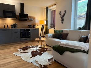 A modern living room with a sofa, a dining table, and a kitchen area with appliances. - Holiday flat Urlaub Schwarzwaldliebe - close to nature! (Bad Teinach-Zavelstein)