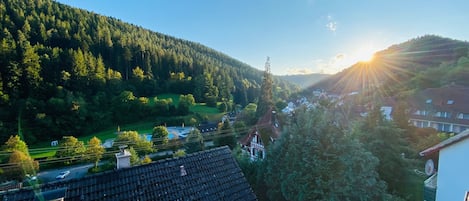 Un quartier résidentiel avec des maisons, un ciel dégagé et un soleil se couchant derrière une colline boisée.