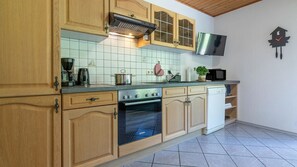 Una cocina con armarios de madera, horno Bosch, microondas y televisor montado en la pared.