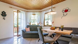 A cozy room with a sofa, a dining table with chairs, a clock, and a wall with a simple design.