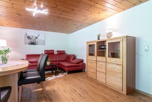 A room with a wooden ceiling, a red leather sofa, a wooden cabinet, and a table with a vase of flowers.
