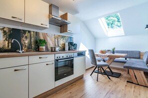Una cocina moderna con horno empotrado, una zona de comedor con un sofá gris y vistas a árboles a través de un tragaluz.