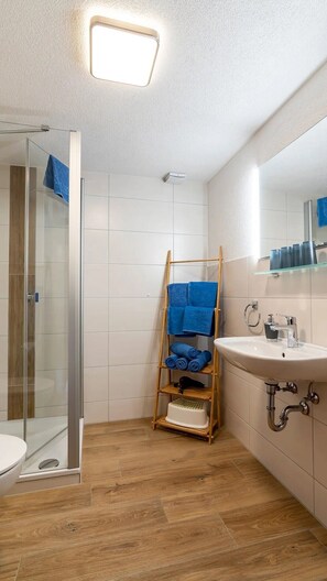Un baño con ducha de vidrio, un perchero de madera, un lavabo y un espejo.