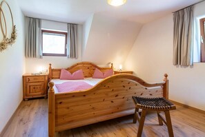 Un dormitorio con cama de madera, una mesita de noche, una silla y una ventana con cortinas.