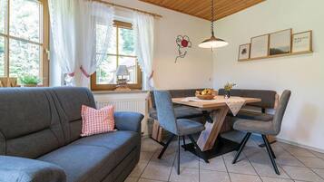 Ein gemütliches Zimmer mit einer grauen Couch, einem Esstisch mit Stühlen, einer Lampe und gerahmten Bildern an der Wand.