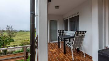 A balcony with a table and chairs, a window with a view of the countryside, and a door leading to the interior.