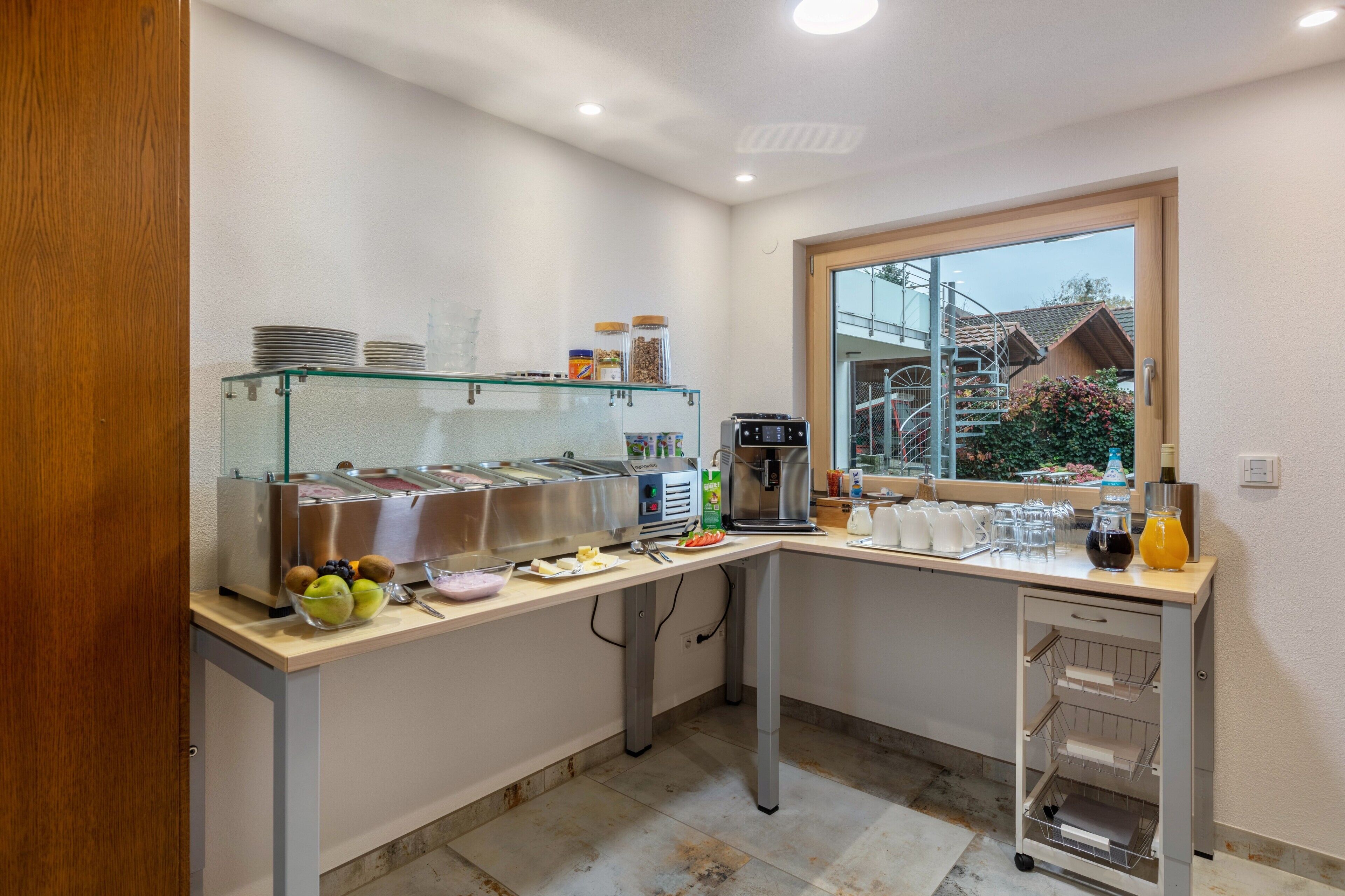 Un bar pour le petit-déjeuner avec une vitrine réfrigérée, une machine à café et une fenêtre donnant sur une maison.