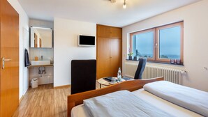 A hotel room with a bed, a desk, a chair, a TV, a window with a view, and a bathroom with a sink and mirror.