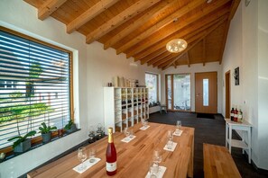 A room with a wooden ceiling, a wine rack, a table set for dining, and a view through large windows.