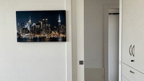Une chambre à coucher avec un tableau représentant un paysage urbain, une armoire et un couloir menant à une autre pièce.