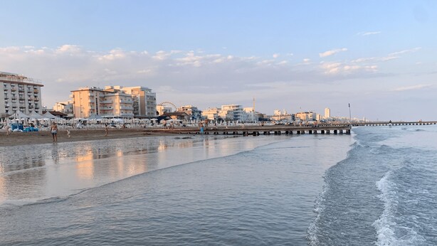 Une plage avec une jetée qui s’avance dans l’eau, une grande roue et des bâtiments en arrière-plan.