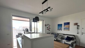 Un salon moderne comprenant un coin repas, un canapé et offrant une vue sur la ville grâce à de grandes fenêtres.