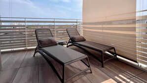 Un balcon avec deux chaises longues, un plancher en bois et une vue sur le paysage urbain.