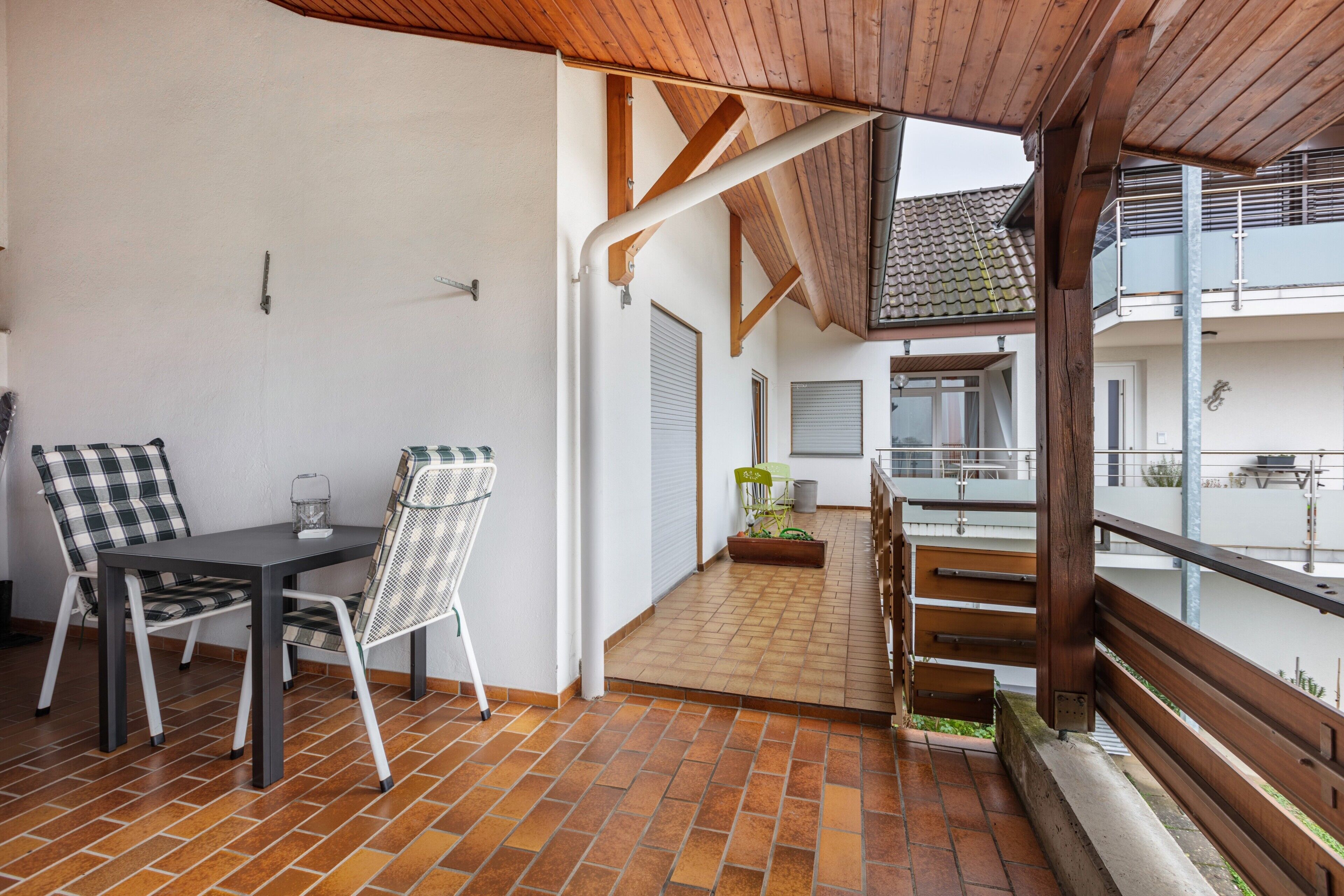En udendørs terrasse med et bord og stole, et trægelænder og udsigt til bygningens indre.