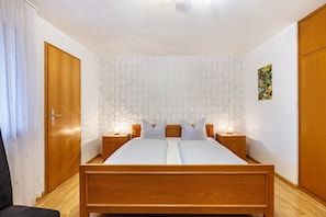 Un dormitorio con una cama de madera, dos mesitas de noche, un aparador, una puerta y una pared con estampado floral.
