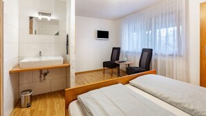 A hotel room with a bed, a bathroom with a sink and mirror, a TV, and a window with curtains. - Room 'Doppelzimmer 3 - Chardonnay' with Shared Terrace, Shared Garden and Wi-Fi (Bad Bellingen)