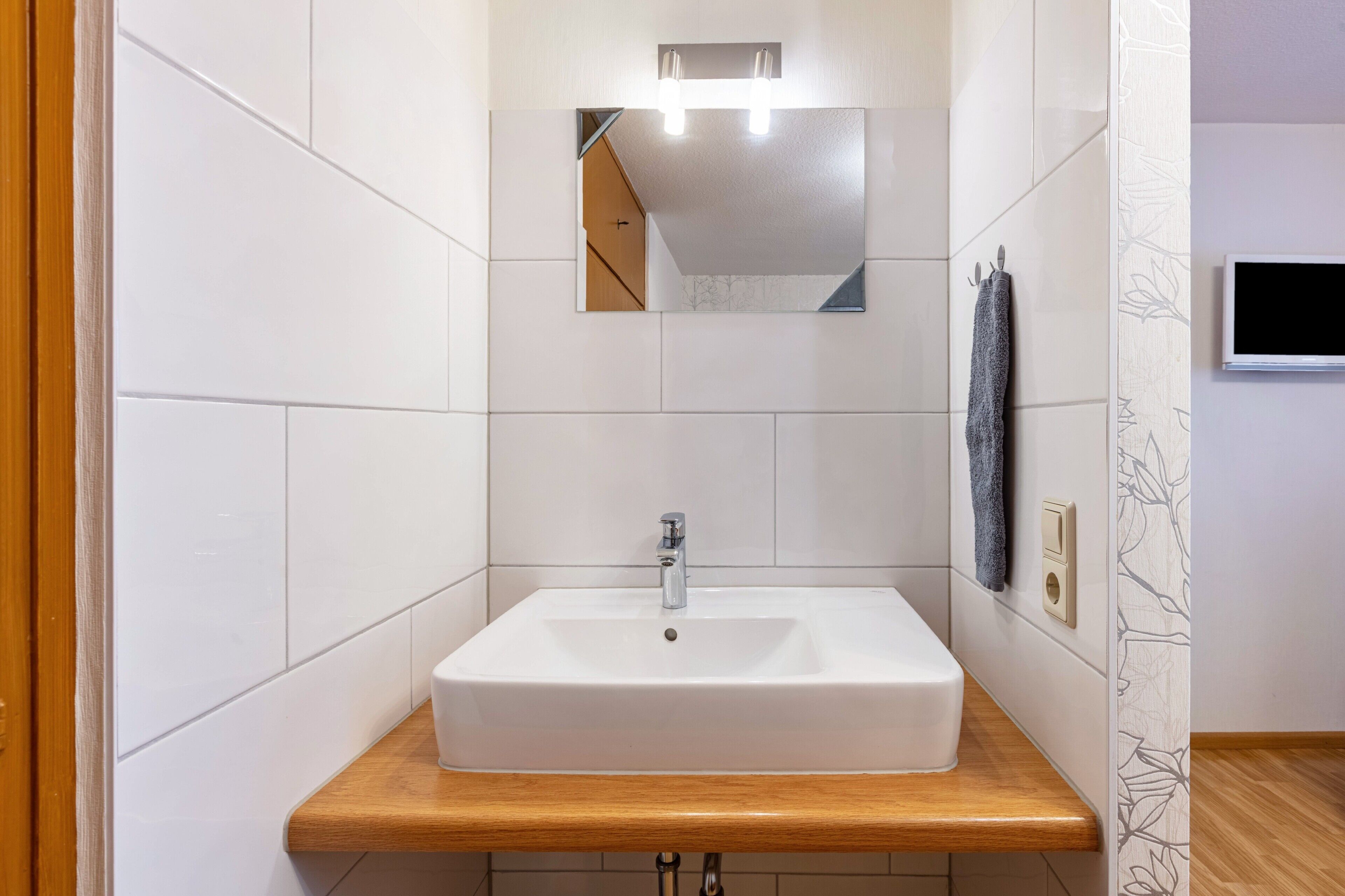 A bathroom with a white sink, wooden countertop, and a mirror with lights above.
