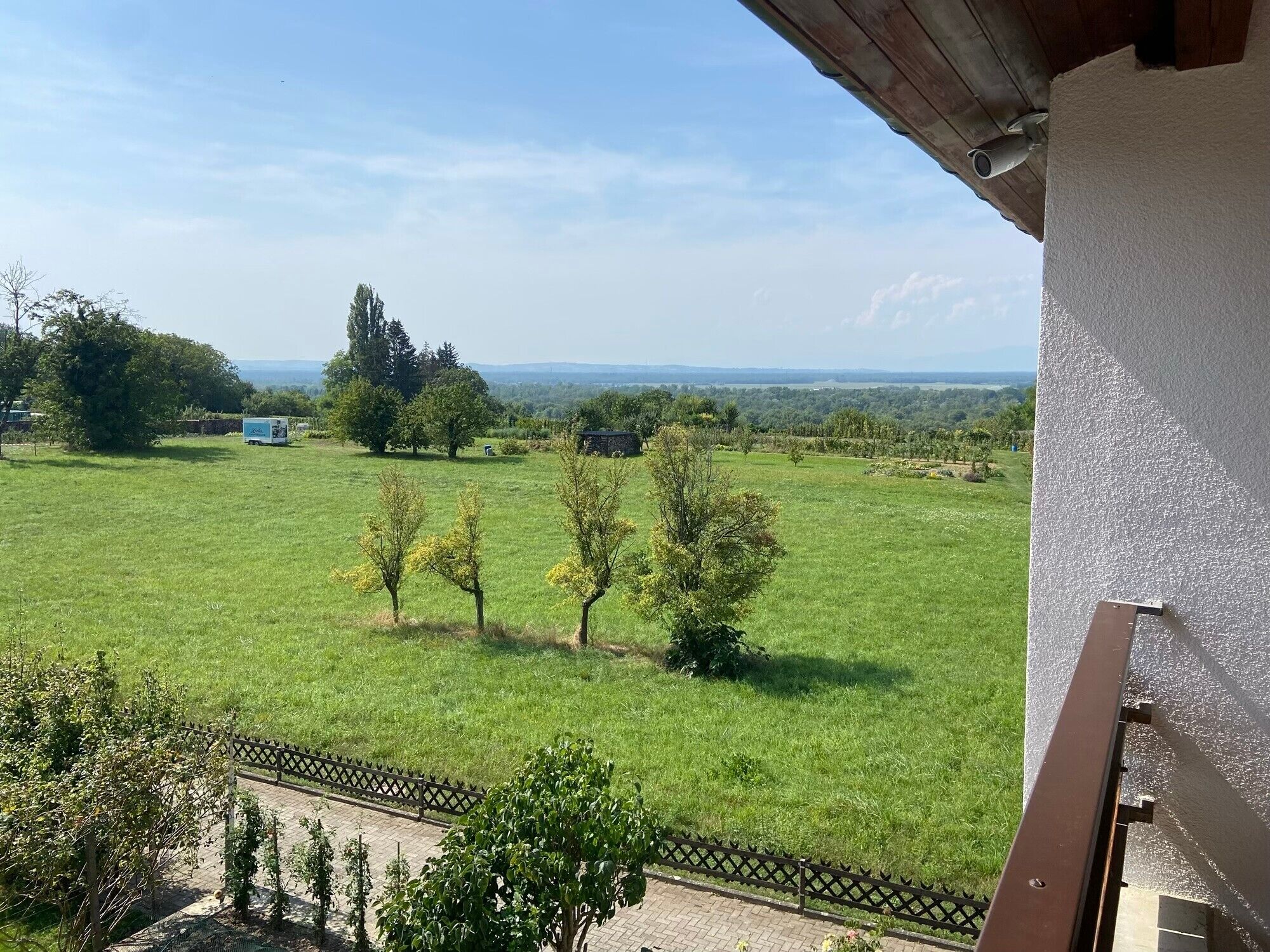 Vista de uma varanda com vista para um campo verde com árvores e horizonte distante.