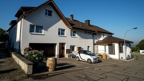 A two-story building with a garage, a white car parked in front, and a small attached structure. - Room 'Doppelzimmer 3 - Chardonnay' with Shared Terrace, Shared Garden and Wi-Fi (Bad Bellingen)