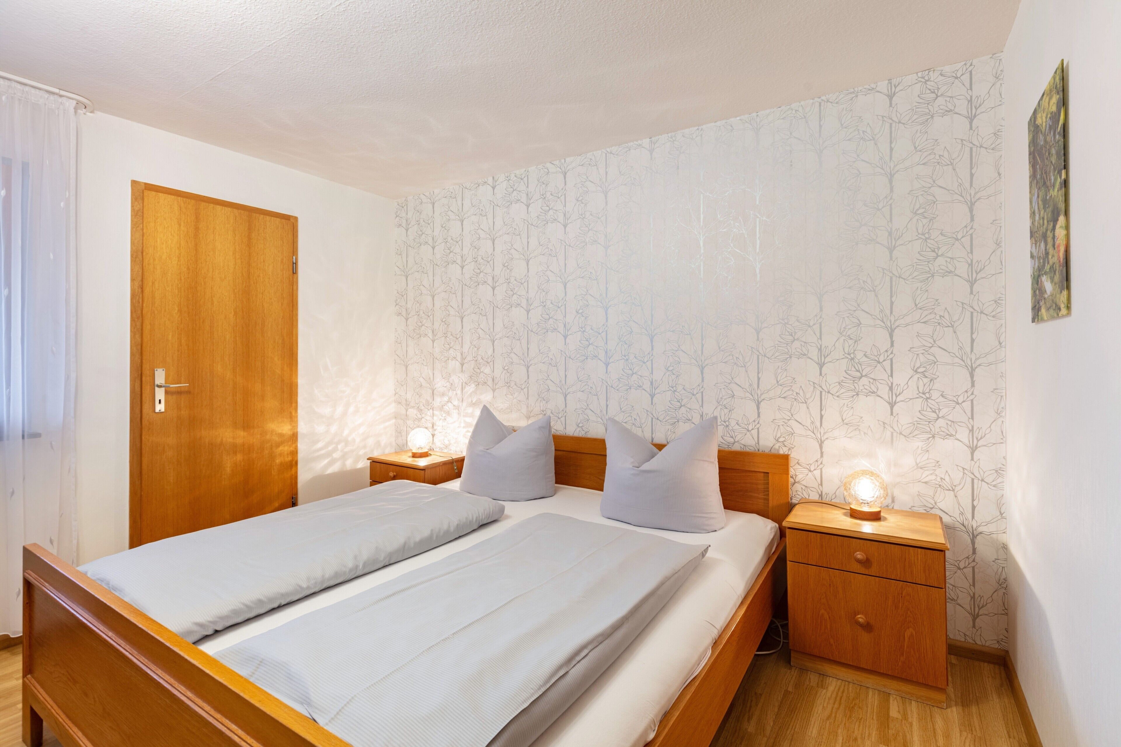 A double bed with two nightstands, a wooden door, and a wall with a tree pattern.
