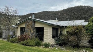 A single-story house with a stone facade and a sloped roof, surrounded by a grassy yard and dense forest. - Enjoy Alpine Lifestyle at Mesley Manor, in heart of Omeo, close to Bike Trails (Omeo)