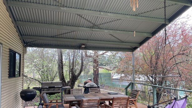 A covered outdoor patio with a wooden table and chairs, a barbecue grill, and a hanging hammock. - Enjoy Alpine Lifestyle at Mesley Manor, in heart of Omeo, close to Bike Trails (Omeo)