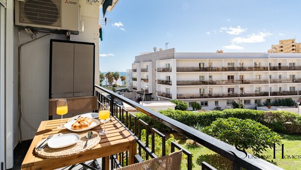 Un balcón con una mesa dispuesta para el desayuno, con vista a un edificio moderno con varios balcones y una vista despejada del mar.
