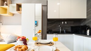 Cocina moderna con armarios blancos, encimera negra y salpicadero de mármol. Hay una mesa con café de la mañana, un croissant, fruta y zumo de naranja.
