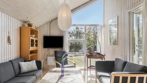 A modern living room with a sofa, armchair, and coffee table. A television is mounted on the wall, and there is a window providing a view of the outdoors.